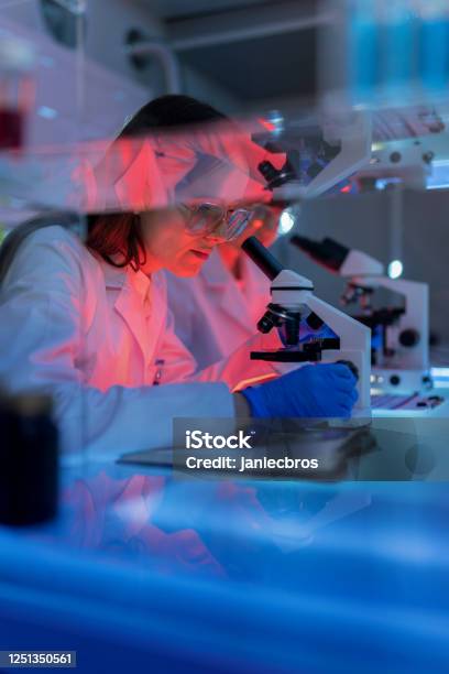 Microbiologist studying pathogen, making notes. Wearing protective workwear